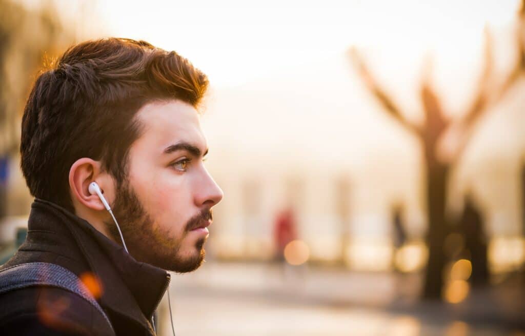 Young man in a city setting intently listening through earphones, a representation of a target audience engaging with content, highlighting the ROI of a branded podcast.