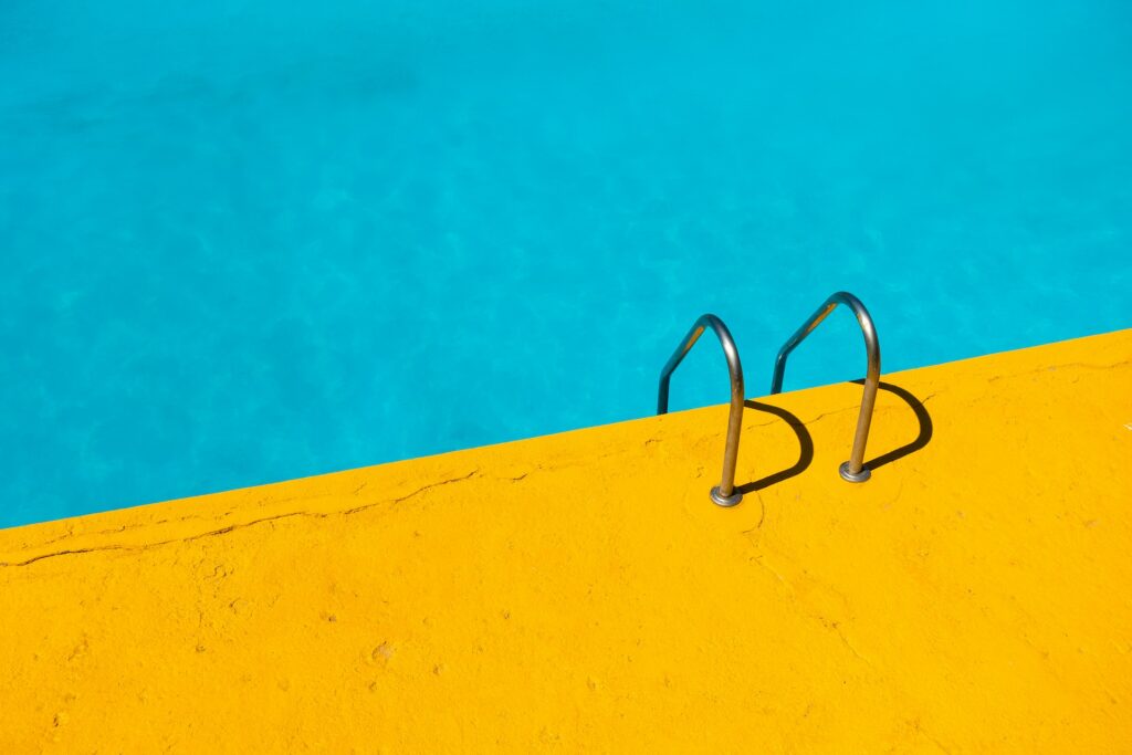 Vibrant image of a pool with bright blue water and a yellow edge, featuring a stainless steel ladder, symbolizing the refreshing and impactful results of the ROI of a branded podcast in marketing strategies.