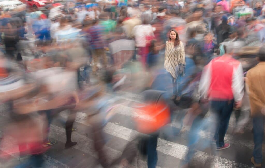 A woman stands still and focused amidst a blurred crowd crossing a busy intersection, symbolizing how the ROI of a branded podcast helps brands stand out in a fast-paced market.
